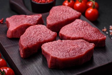 Tuz, baharat ve otlarla sulu taze çiğ et, koyu dokulu beton arka planda.