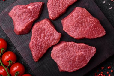 Tuz, baharat ve otlarla sulu taze çiğ et, koyu dokulu beton arka planda.