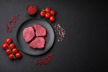 Tuz, baharat ve otlarla sulu taze çiğ et, koyu dokulu beton arka planda.