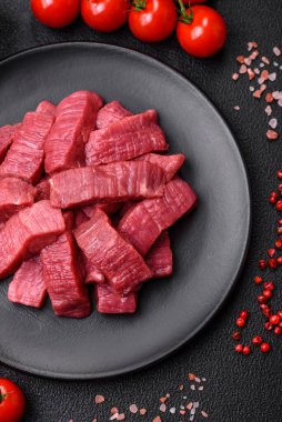 Tuz, baharat ve otlarla sulu taze çiğ et, koyu dokulu beton arka planda.