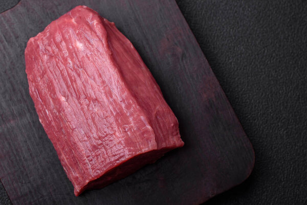 Juicy fresh raw beef meat with salt, spices and herbs on a dark textured concrete background
