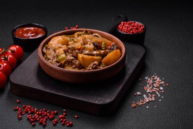 Lezzetli taze patates güveci, domates, soğan, havuç ve tuzlu et, baharat ve çimento arka planda bulunan otlar.