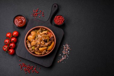 Lezzetli taze patates güveci, domates, soğan, havuç ve tuzlu et, baharat ve çimento arka planda bulunan otlar.