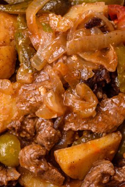 Lezzetli taze patates güveci, domates, soğan, havuç ve tuzlu et, baharat ve çimento arka planda bulunan otlar.