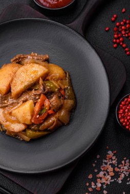 Lezzetli taze patates güveci, domates, soğan, havuç ve tuzlu et, baharat ve çimento arka planda bulunan otlar.