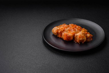 Lezzetli taze deniz balığı parçalara ayrılmış ve koyu beton arka planda tuz, baharat ve otlarla domates sosunda pişirilmiş.