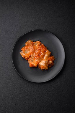 Lezzetli taze deniz balığı parçalara ayrılmış ve koyu beton arka planda tuz, baharat ve otlarla domates sosunda pişirilmiş.