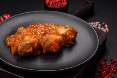 Lezzetli taze deniz balığı parçalara ayrılmış ve koyu beton arka planda tuz, baharat ve otlarla domates sosunda pişirilmiş.