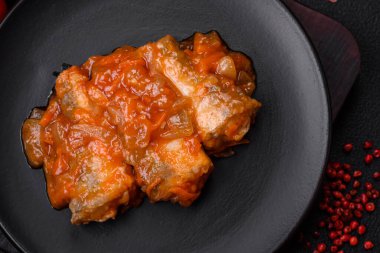 Lezzetli taze deniz balığı parçalara ayrılmış ve koyu beton arka planda tuz, baharat ve otlarla domates sosunda pişirilmiş.