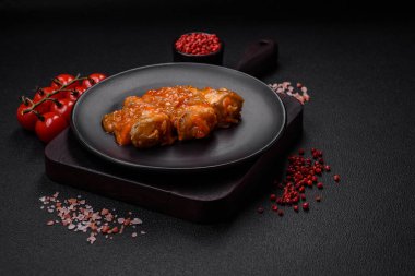 Lezzetli taze deniz balığı parçalara ayrılmış ve koyu beton arka planda tuz, baharat ve otlarla domates sosunda pişirilmiş.