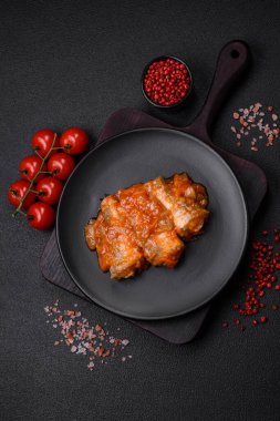 Lezzetli taze deniz balığı parçalara ayrılmış ve koyu beton arka planda tuz, baharat ve otlarla domates sosunda pişirilmiş.