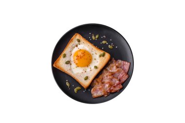 Kalp şeklinde kızarmış yumurta ve susamlı tost, keten tohumu ve balkabağı çekirdeği siyah bir tabakta koyu beton arka planda.