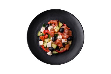 Delicious fresh Greek salad with olives, tomatoes, cucumbers, feta cheese, spices, herbs and olive oil on a black ceramic plate