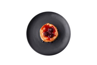 Delicious fresh pancakes with berry jam on a black ceramic plate on a dark concrete background