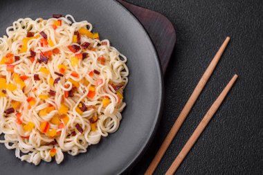 Lezzetli taze Asya erişteleri, sebze parçaları, et, tuz, baharat ve otlarla birlikte koyu beton bir arka planda.