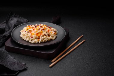 Lezzetli taze Asya erişteleri, sebze parçaları, et, tuz, baharat ve otlarla birlikte koyu beton bir arka planda.