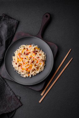 Lezzetli taze Asya erişteleri, sebze parçaları, et, tuz, baharat ve otlarla birlikte koyu beton bir arka planda.