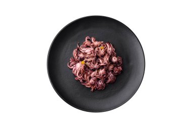 Delicious marinated octopus babies with lemon, salt and spices on a black plate on a dark concrete background
