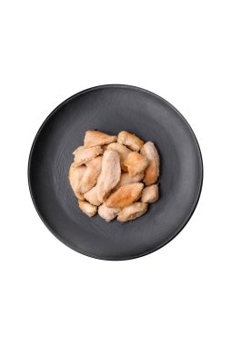 Yuvarlak bir seramik tabakta koyu beton arka planda baharat ve otlarla pişirilmiş lezzetli tavuk dilimleri.