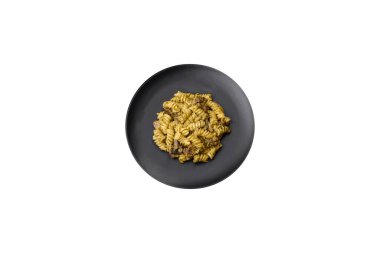 Yeşil pesto soslu lezzetli fusilli makarna, koyu beton bir zeminde seramik tabakta tuz ve baharatlar.