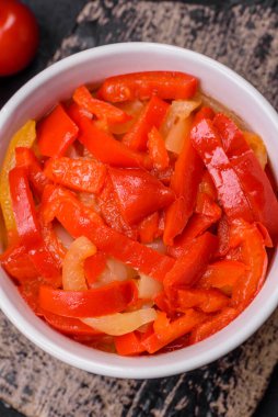 Lezzetli taze sote tatlı dolmalık biber dilimleri soğan, tuz, baharat ve otlar ile koyu beton arka planda.