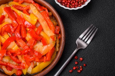 Lezzetli taze sote tatlı dolmalık biber dilimleri soğan, tuz, baharat ve otlar ile koyu beton arka planda.