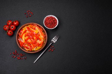 Lezzetli taze sote tatlı dolmalık biber dilimleri soğan, tuz, baharat ve otlar ile koyu beton arka planda.