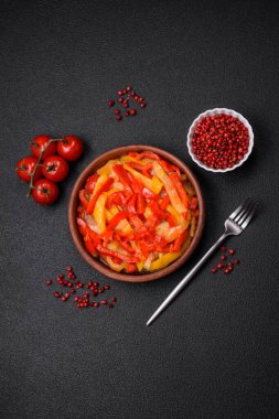 Lezzetli taze sote tatlı dolmalık biber dilimleri soğan, tuz, baharat ve otlar ile koyu beton arka planda.