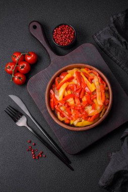 Lezzetli taze sote tatlı dolmalık biber dilimleri soğan, tuz, baharat ve otlar ile koyu beton arka planda.