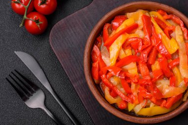 Lezzetli taze sote tatlı dolmalık biber dilimleri soğan, tuz, baharat ve otlar ile koyu beton arka planda.