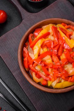 Lezzetli taze sote tatlı dolmalık biber dilimleri soğan, tuz, baharat ve otlar ile koyu beton arka planda.