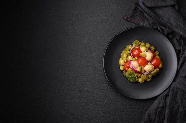 Brokolili taze salata, kiraz domatesleri, mantarlar, soğanlar, tuz, baharatlar ve koyu beton arka planda otlar.