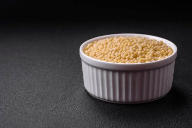 Koyu beton arka planda seramik bir kasede çiğ ptitim makarna. İsrail gıda hazırlığı