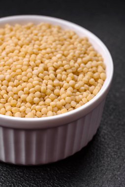 Koyu beton arka planda seramik bir kasede çiğ ptitim makarna. İsrail gıda hazırlığı