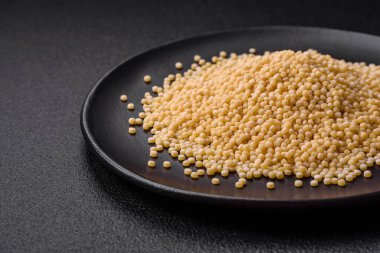 Koyu beton arka planda seramik bir kasede çiğ ptitim makarna. İsrail gıda hazırlığı