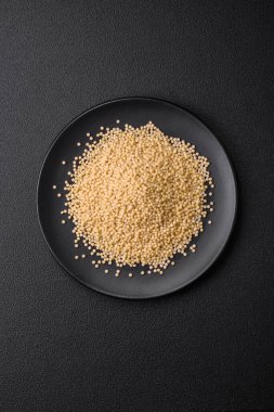 Koyu beton arka planda seramik bir kasede çiğ ptitim makarna. İsrail gıda hazırlığı