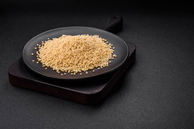 Koyu beton arka planda seramik bir kasede çiğ ptitim makarna. İsrail gıda hazırlığı