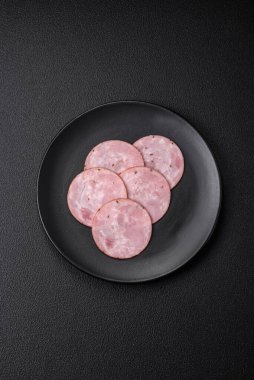 Lezzetli taze jambon, tuz, baharat ve otlarla kesilmiş koyu beton arka planda yuvarlak dilimler halinde.