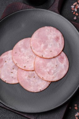 Lezzetli taze jambon, tuz, baharat ve otlarla kesilmiş koyu beton arka planda yuvarlak dilimler halinde.