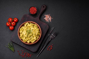 Pesto soslu lezzetli taze makarna, tuz, baharatlar ve çimento kaplı seramik bir tabakta otlar.