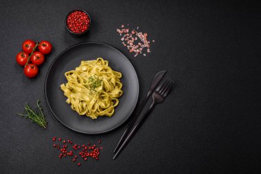 Pesto soslu lezzetli taze makarna, tuz, baharatlar ve çimento kaplı seramik bir tabakta otlar.