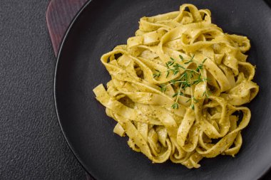 Pesto soslu lezzetli taze makarna, tuz, baharatlar ve çimento kaplı seramik bir tabakta otlar.