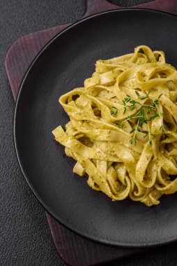Pesto soslu lezzetli taze makarna, tuz, baharatlar ve çimento kaplı seramik bir tabakta otlar.