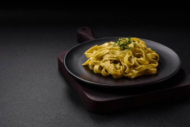 Pesto soslu lezzetli taze makarna, tuz, baharatlar ve çimento kaplı seramik bir tabakta otlar.