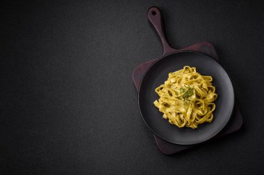 Pesto soslu lezzetli taze makarna, tuz, baharatlar ve çimento kaplı seramik bir tabakta otlar.