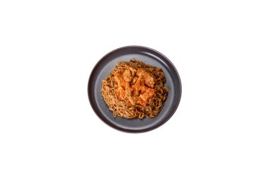 Plate of fried noodles and vegetables with hot chicken sauce on restaurant table, chinese cuisine