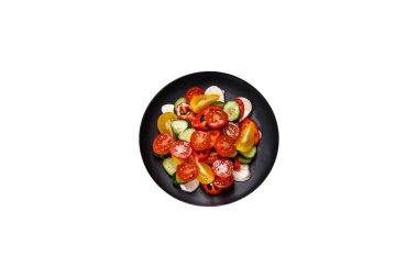 Fresh, delicious salad with cherry tomatoes, cucumbers, sweet peppers, cheese and olive oil on a black plate against a dark concrete background. Vegetarian dish