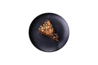 A piece of fresh delicious cake with nuts and chocolate on a black plate against a dark blue background. Desserts and sweets to the dinner table