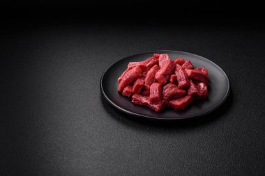 Raw organic meat beef or lamb cut into slices with salt, spices and herbs on a dark concrete background clipart