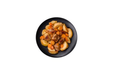 Beef meat and vegetables stew on a black plate with roasted potatoes. Dark background. Copy space